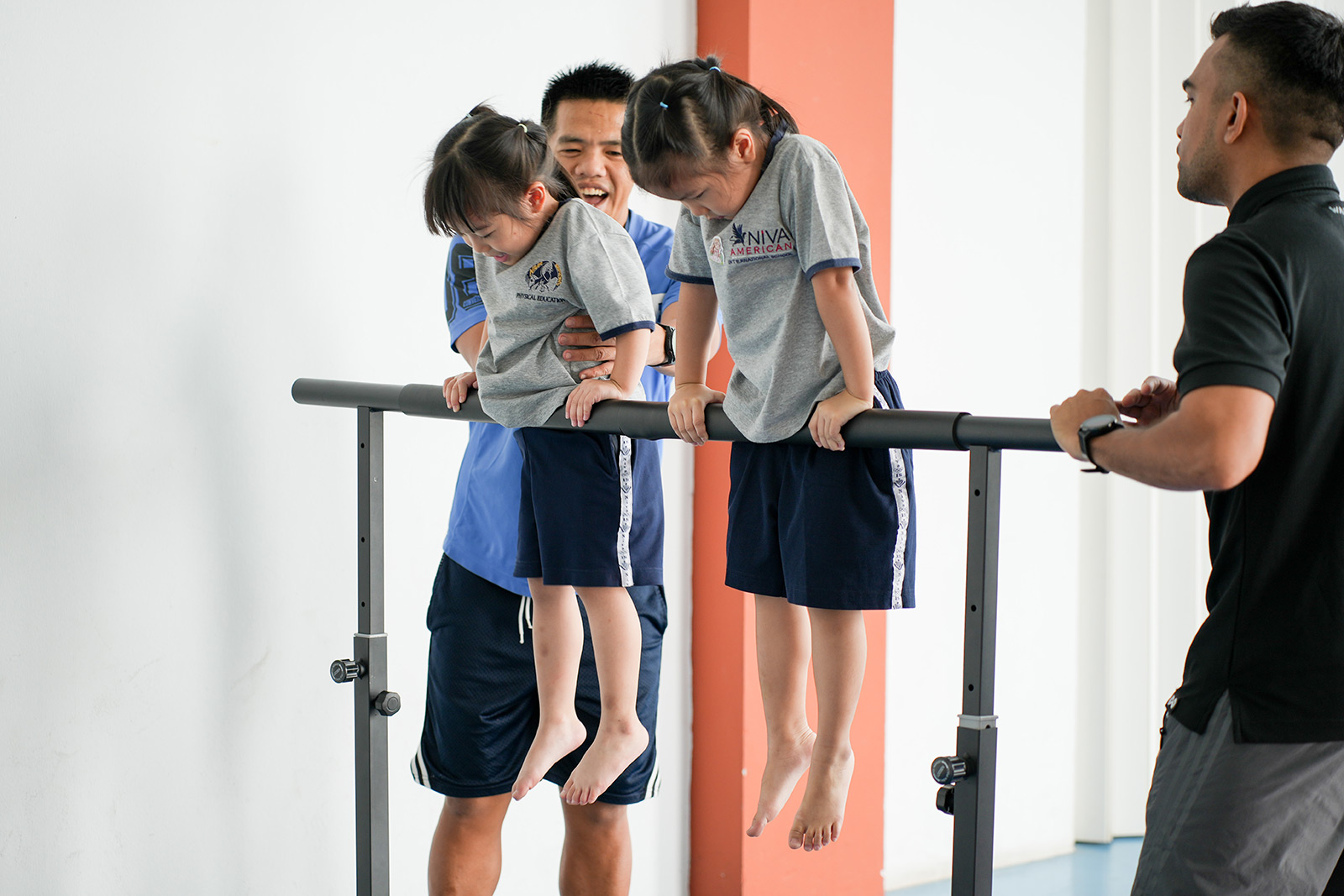 Kindergarten students hanging from a bar with a teacher nearby