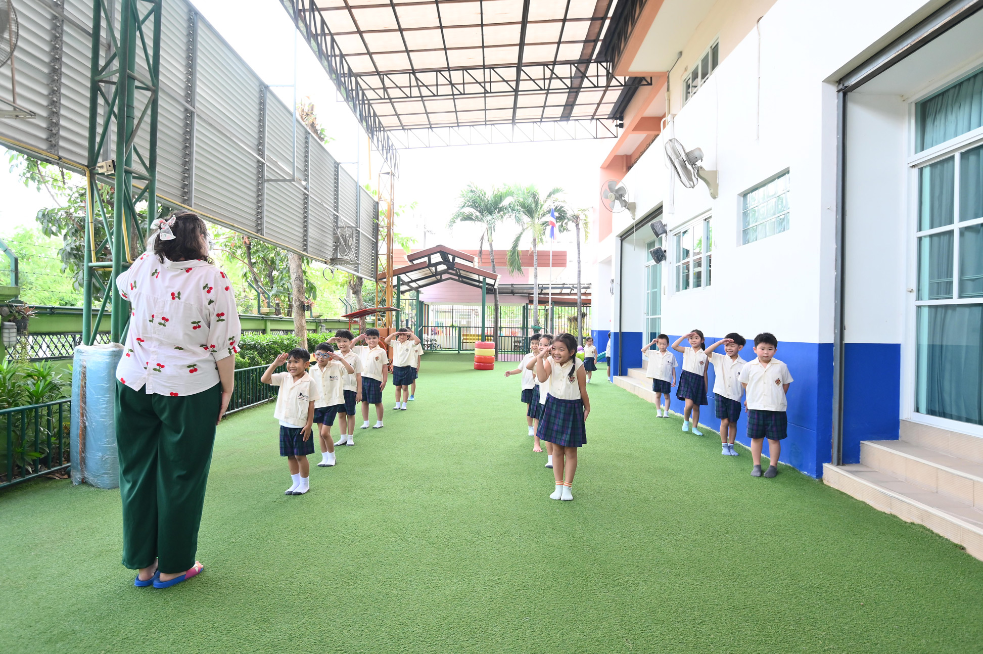 Kindergarten students lining up beside a teacher outdoors