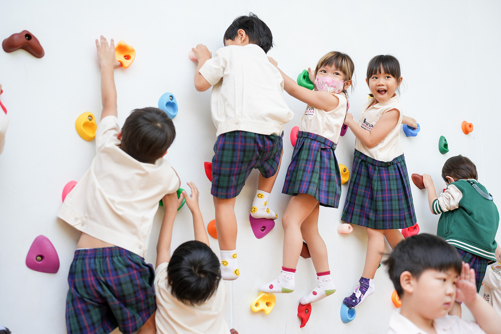 Kindergarten students climbing a wall with teachers nearby