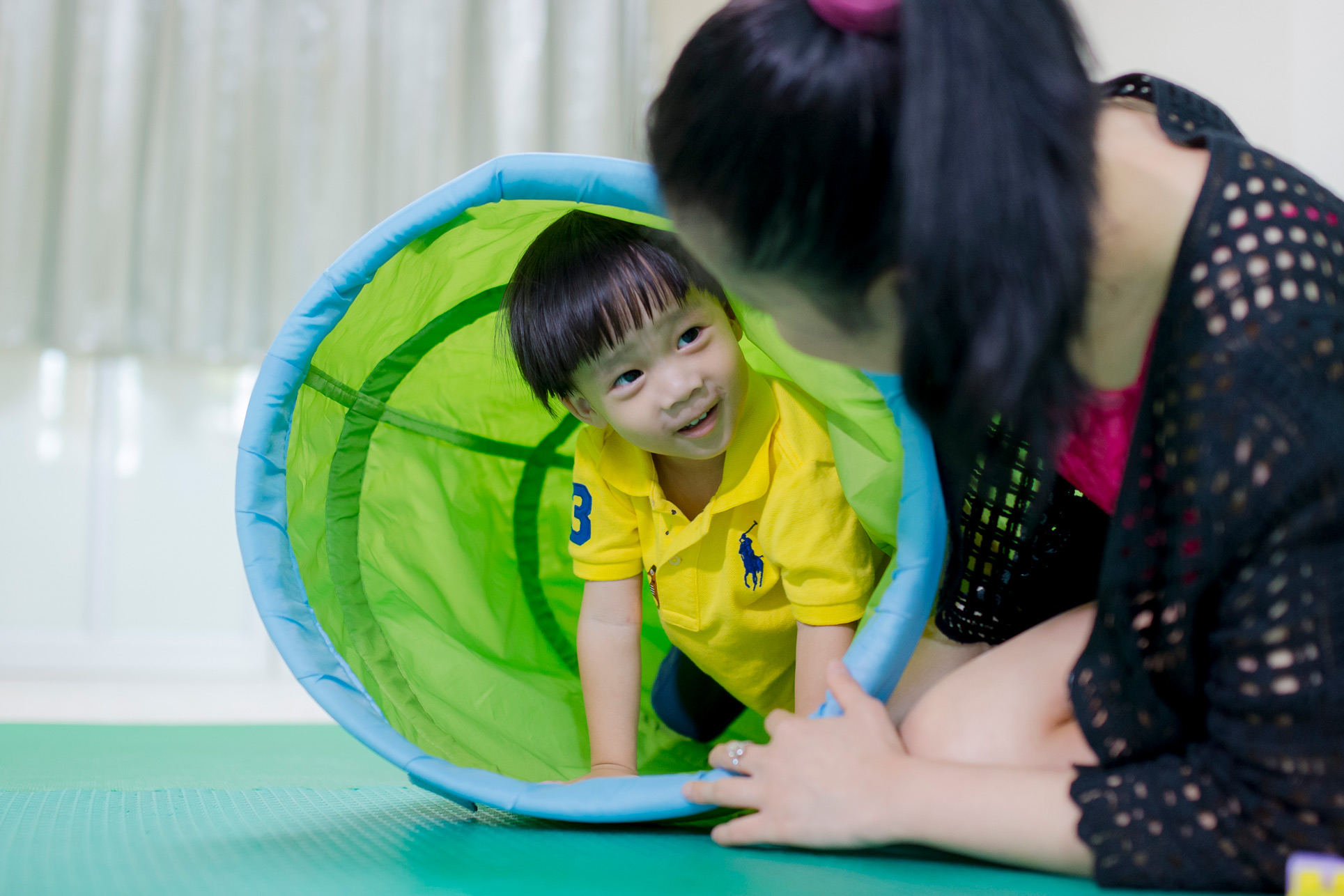 Nursery child crawling through a play tunnel with a teacher nearby