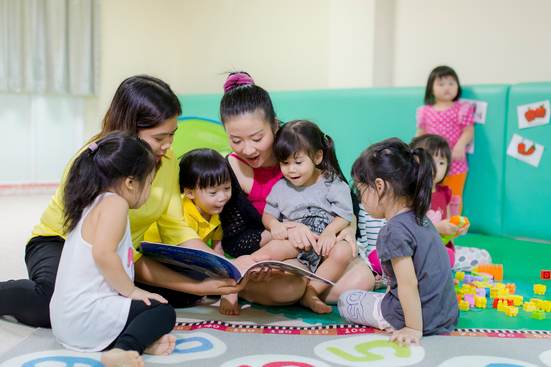 Nursery teachers reading with children on the classroom floor