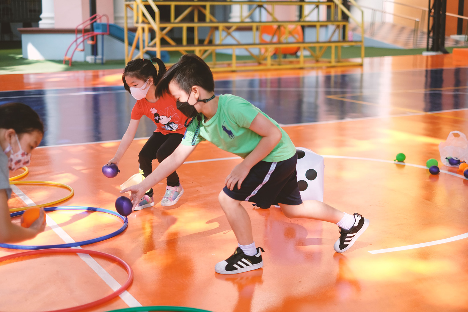 เด็กเล่นเกมกับห่วงและลูกบอลหลากสีบนสนาม